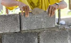 Murarz układa bloczek betonowy, dbając o jego wymiary i równość.