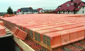 Strop ackermana w budowie, rzędy pustaków ceramicznych czekają na zalanie betonem. W tle domy z czerwonymi dachami.