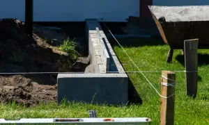 Budowa fundamentu pod ogrodzenie z bloczków betonowych. Widać poziomicę, sznur i taczkę w tle.