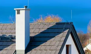 Biały komin i dachówka na dachu domu, z widocznym systemem piorunochronu chroniącym przed burzą.