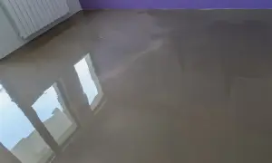 Lśniąca, szara wylewka w nowym pomieszczeniu, odbijająca światło z okien.