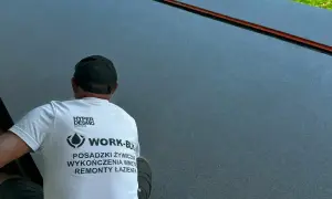 Pracownik w koszulce z napisem "POSADZKI ŻYWICZNE" wykonuje prace na gładkiej, ciemnej powierzchni.