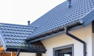 Szary dach z dachówki ceramicznej, rynny i komin. Sprawdź, jaka jest dachówka ceramiczna cena za m2.