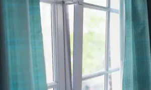 Okna z białymi szprosami, zasłonięte turkusowymi zasłonami w kratkę.