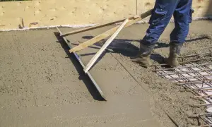 Pracownik wykonuje szlifowanie betonu za pomocą łaty, wyrównując świeżą nawierzchnię.