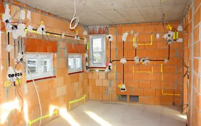 Rozpoczyna się instalacja elektryczna w nowym budynku. Widać przewody, puszki i oznaczenia na ceglanych ścianach.