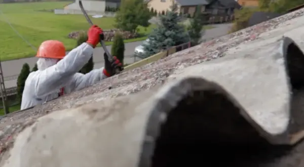 Osoba w kombinezonie i kasku usuwa eternit z dachu. To pokazuje, co to jest azbest i jak niebezpieczny może być.