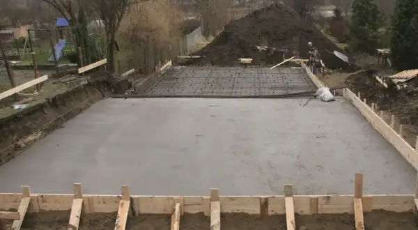 Plac budowy z wylana płytą betonową, przygotowywaną pod fundamenty. Widoczne zbrojenie i szalunki. Klasy ekspozycji betonu są kluczowe dla trwałości.