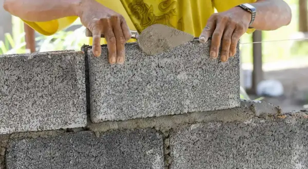 Murarz układa bloczek betonowy, dbając o jego wymiary i równość.