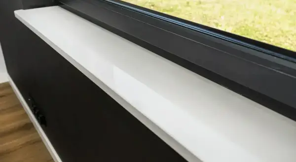 Biały parapet z konglomeratu pod czarną ramą okna, z widokiem na zielony trawnik.