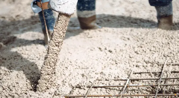 Beton wylewany z rury na zbrojenie, w tle widać nogi w gumowcach.