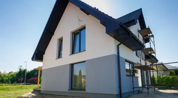 Nowy dom z dwukolorową elewacją, biało-szarą, to świetny pomysł na elewację domu. Widać rusztowania, co sugeruje trwające prace.