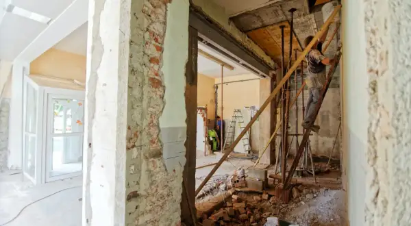 Trwa remont starego domu. Widać rozbiórkę ścian, rusztowania i robotników.