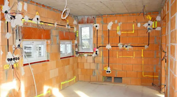 Rozpoczyna się instalacja elektryczna w nowym budynku. Widać przewody, puszki i oznaczenia na ceglanych ścianach.