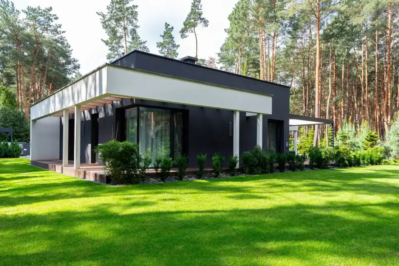 Nowoczesny dom z dużymi oknami i tarasem, otoczony zielonym ogrodem. Szacowany koszt budowy domu 220m2.