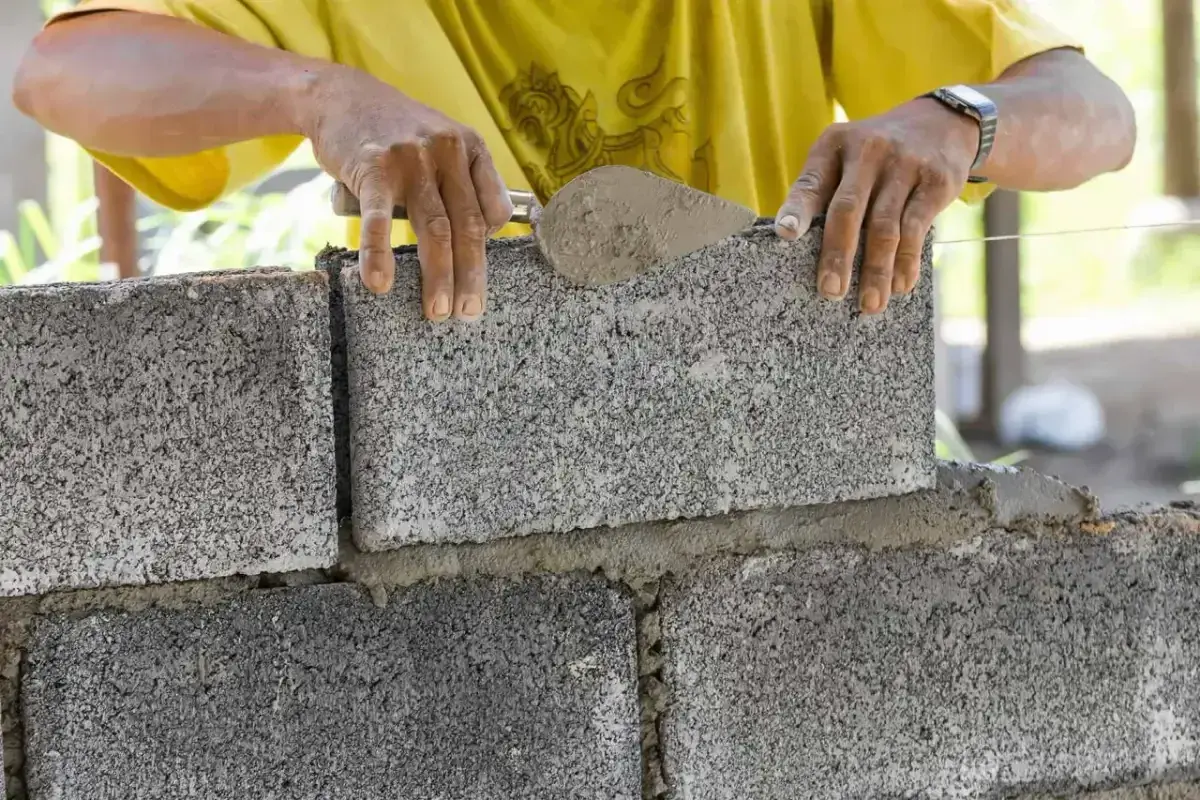 Murarz układa bloczek betonowy, dbając o jego wymiary i równość.