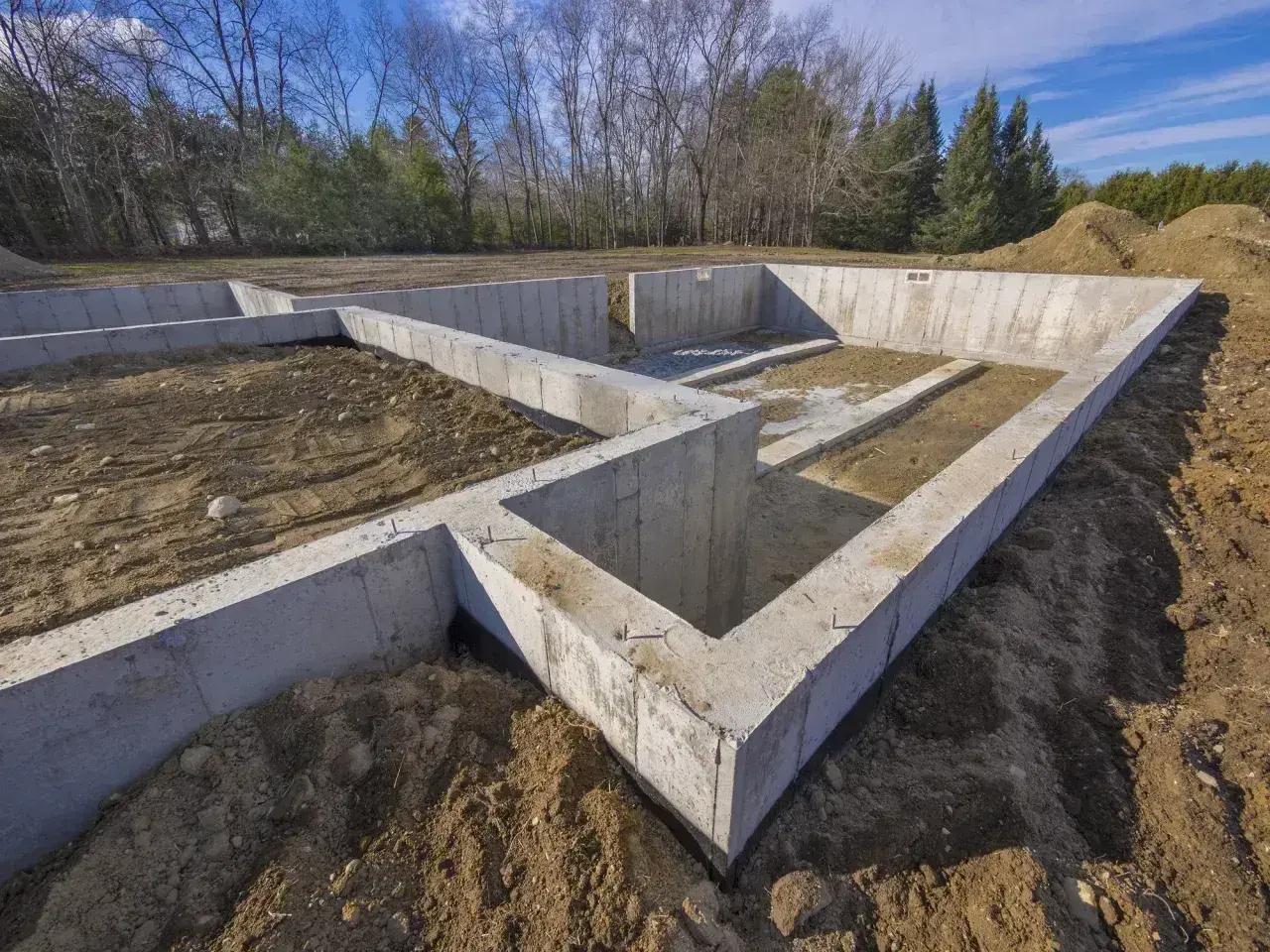 Betonowy fundament domu w budowie, otoczony ziemią i drzewami. Solidny fundament to podstawa każdej budowli.