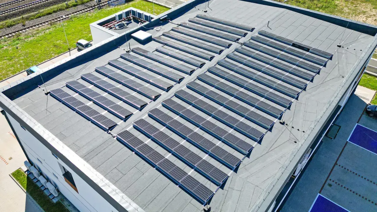 Duży dach płaski pokryty panelami fotowoltaicznymi, które zbierają energię słoneczną.