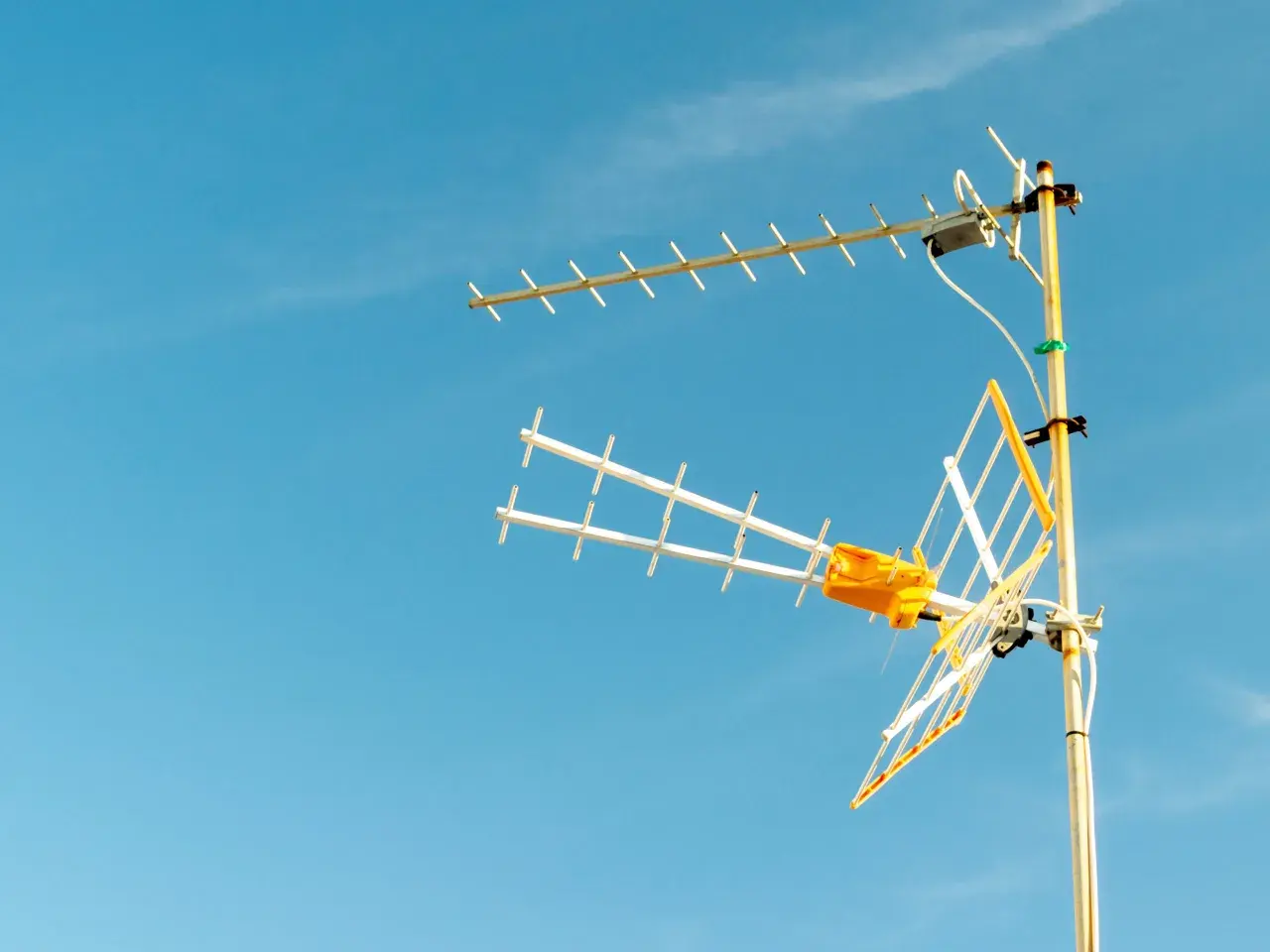 Antena TV z żółtym elementem na tle błękitnego nieba.