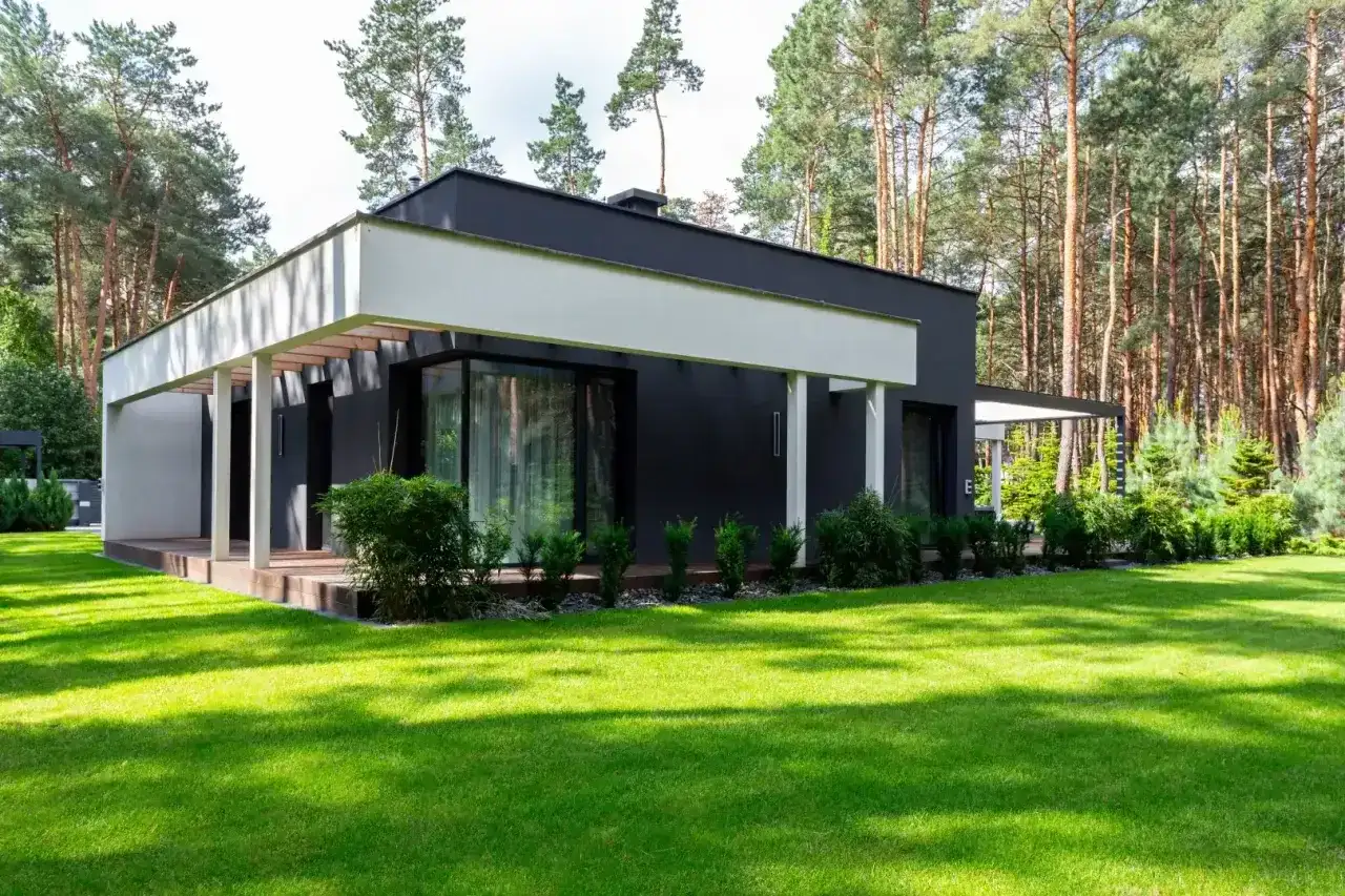 Nowoczesny dom z dużymi oknami i tarasem, otoczony zielonym ogrodem. Szacowany koszt budowy domu 220m2.