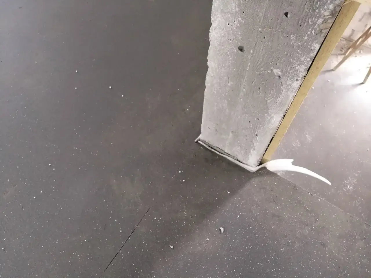 Szara podłoga z widoczną dylatacją przy betonowym słupie, uszczelnioną białą masą.