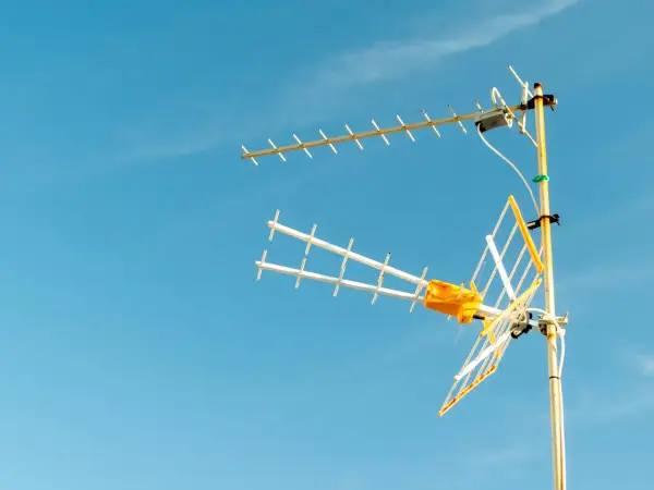 Antena TV z żółtym elementem na tle błękitnego nieba.