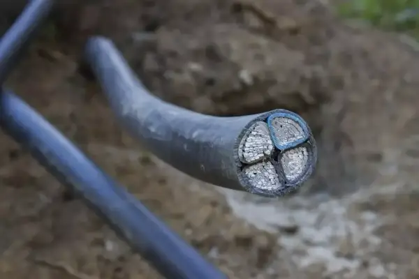 Przekrój grubego kabla energetycznego z czterema żyłami, widoczny w ziemi. Arot przewodów jest solidny.