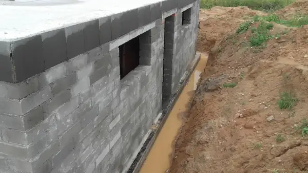 Budowa domu w toku. Widać fundamenty z bloczków, okna i rozpoczęty drenaż opaskowy odprowadzający wodę z wykopu.